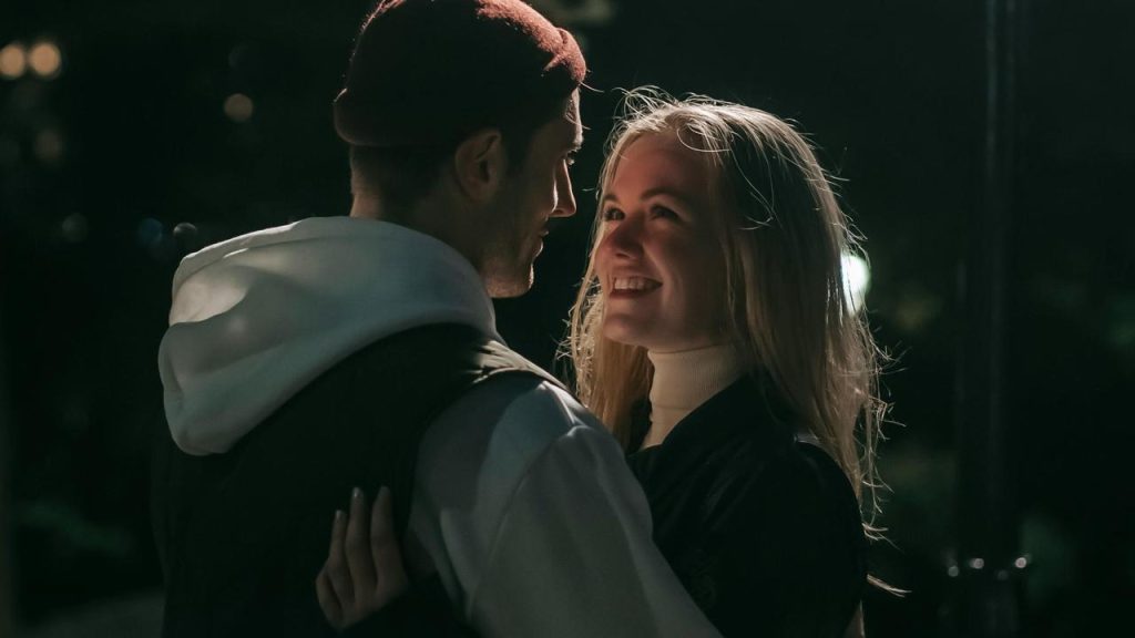 A couple embracing and smiling at each other outdoors at night.