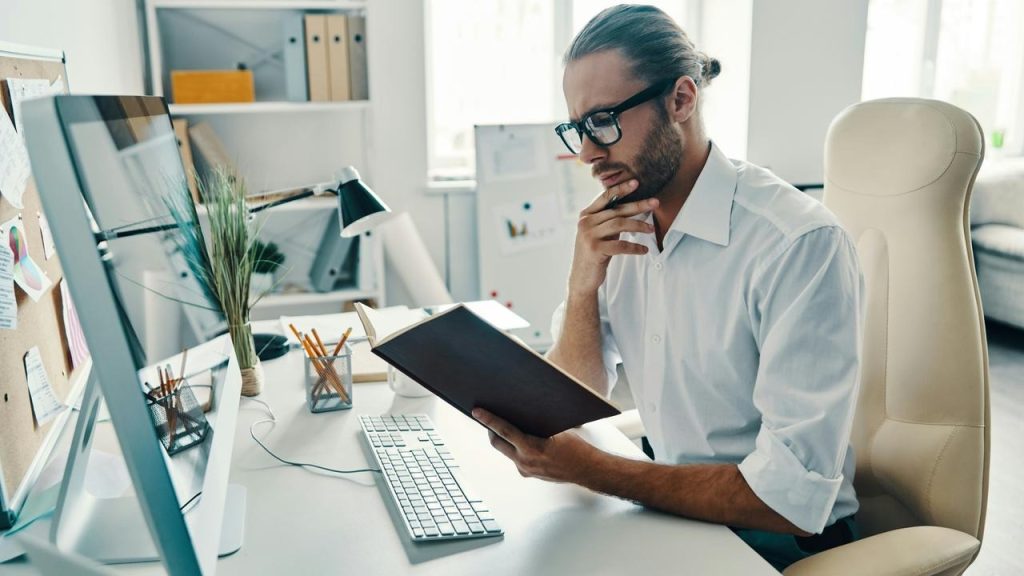 A man in an office reading a notebook at his desk.