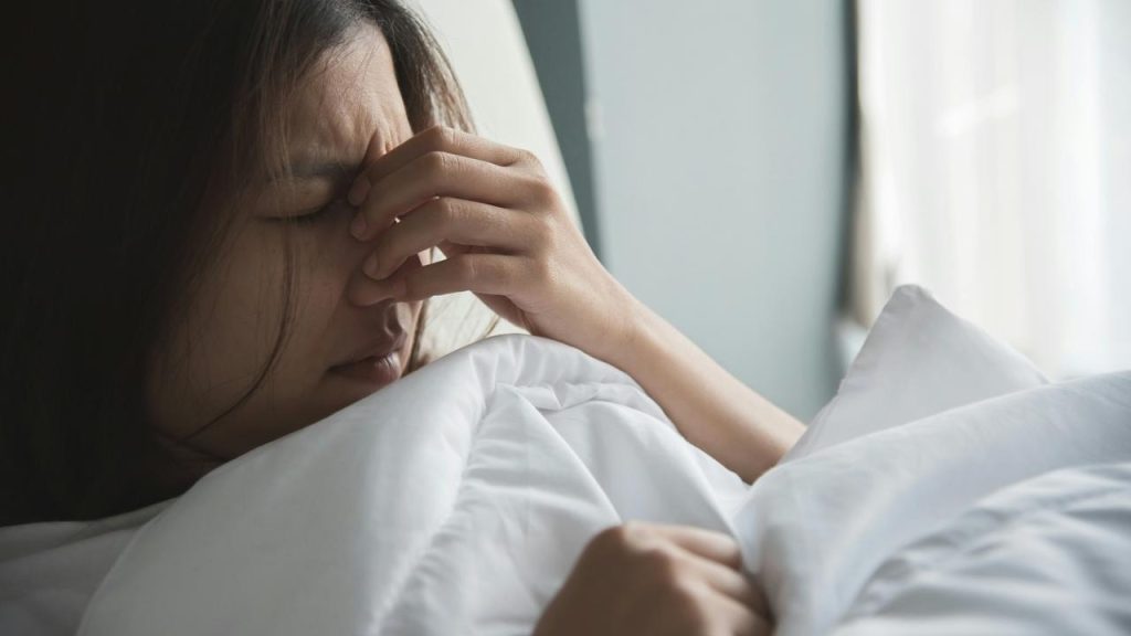 A tired woman in bed holding her face as if in pain or stress.
