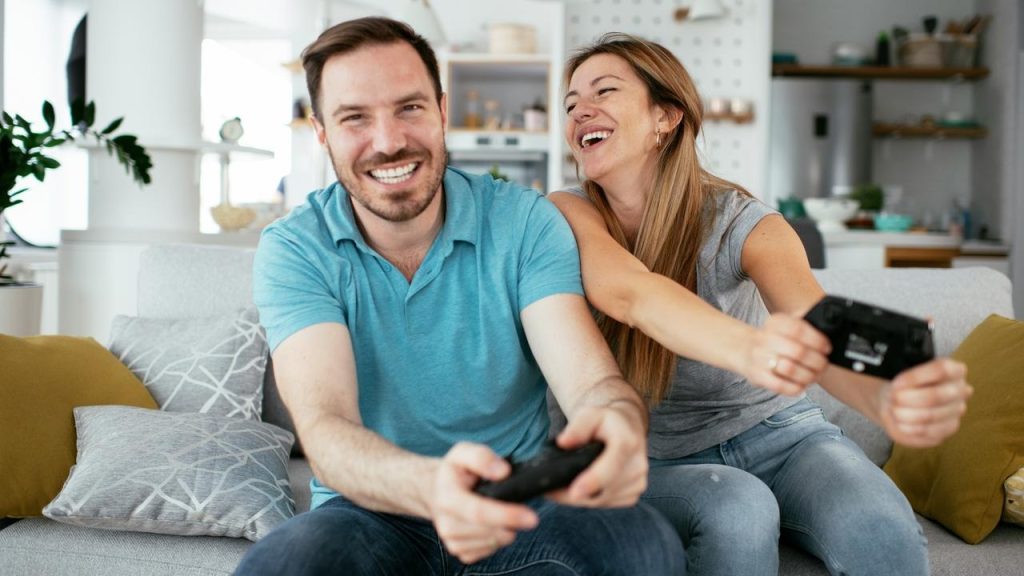A smiling couple sitting on a couch playing video games together.
