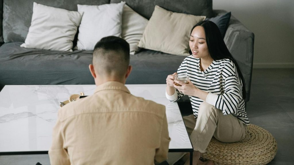 A woman sitting on the floor in a living room with a man and holding a cup of coffee.