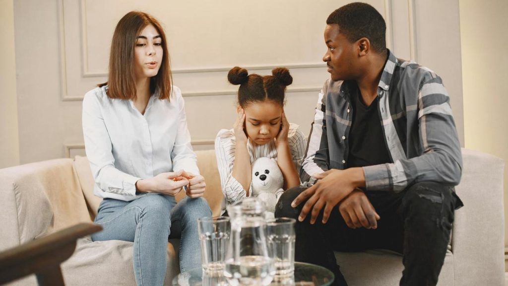 A couple with a young girl holding a stuffed toy during a serious conversation.