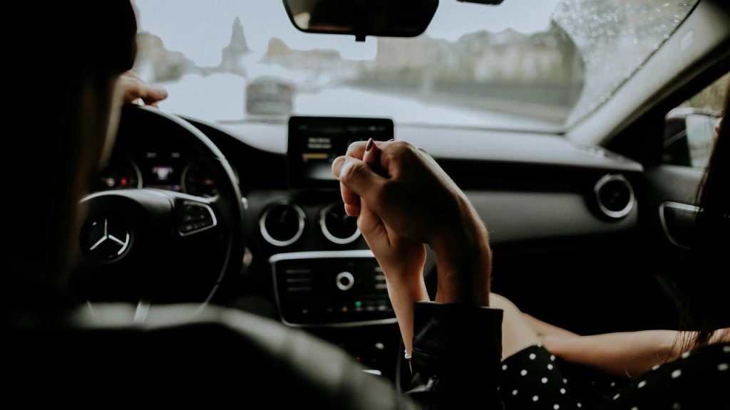 A couple holding hands inside a car while driving in rainy weather.