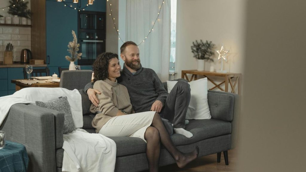 A couple sitting close together on a couch, smiling in a cozy living room.