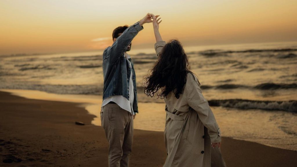 A couple dancing on a beach at sunset by the ocean.