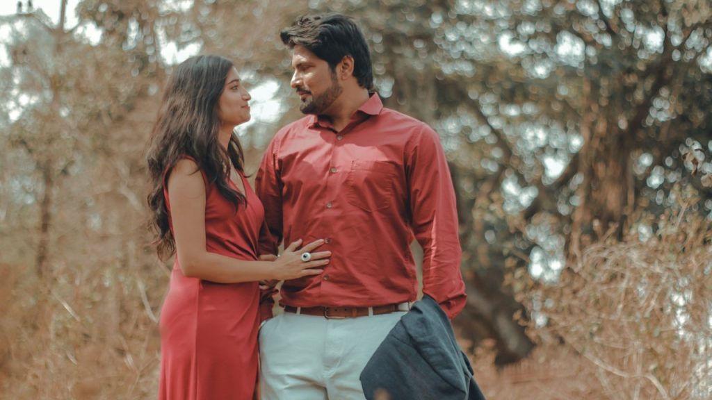 A man and a woman in red dresses are standing in a forest.