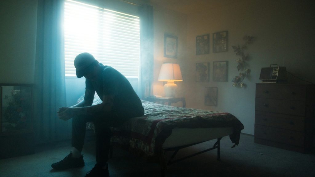 A man in a black jacket sitting on a bed.