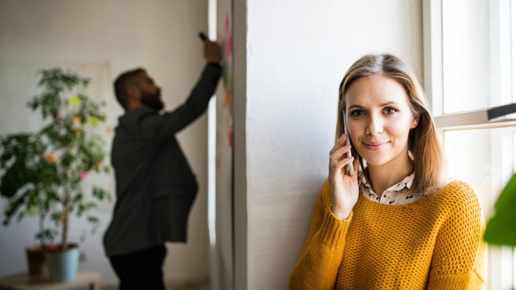 Two businesspeople in the office are working together—a woman with a smartphone making a phone call.