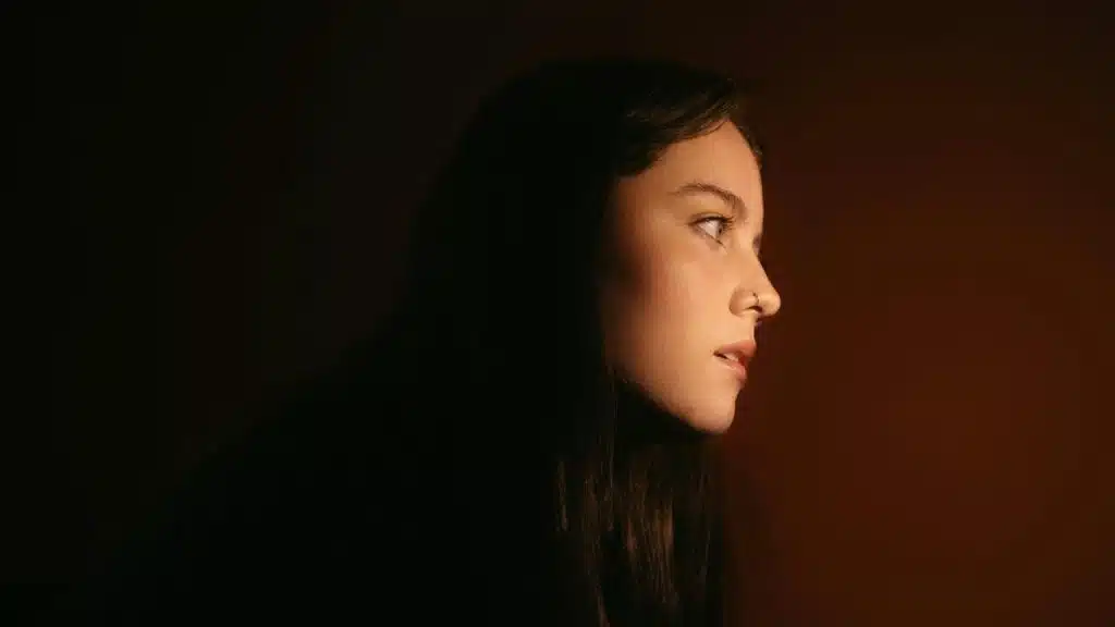 A woman in profile lit softly against a dark background.