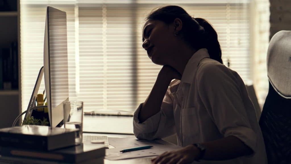 A person slumped at a desk, resting their head beside a computer screen.