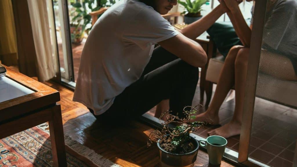 A couple sitting closely indoors, holding hands during a quiet moment.
