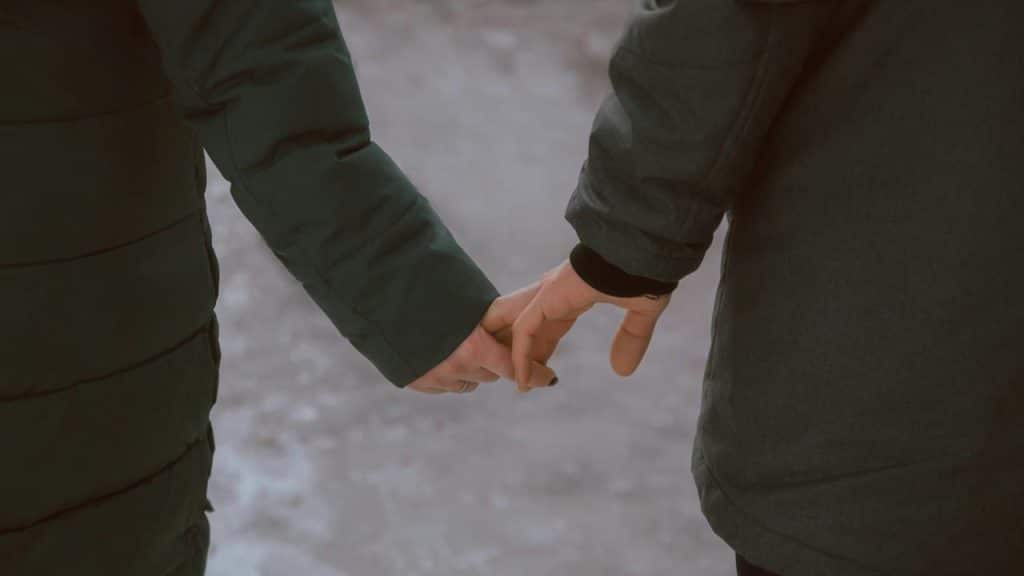 A close-up of two people holding hands while walking outdoors in winter coats.