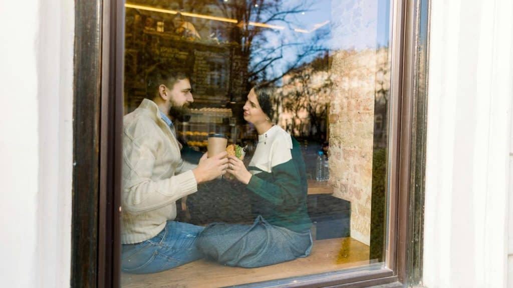 A couple sharing coffee inside a café by a window.