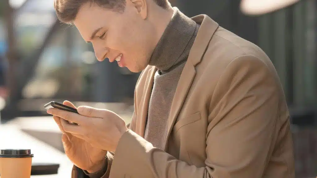 A man smiling while using his phone at an outdoor café.