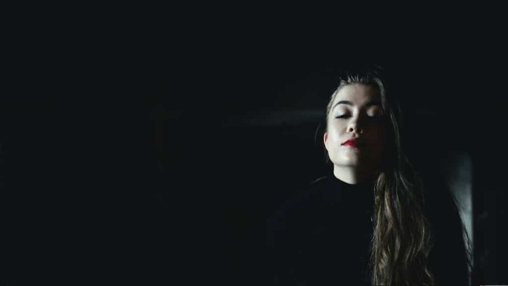 A woman wearing a black crew-neck top inside a black room.