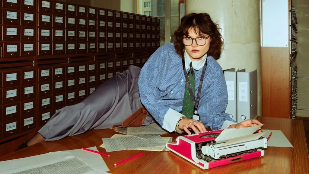 A woman wearing glasses is typing on an old typing machine.