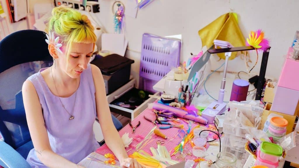 A woman wearing a funky dress is making handmade cards while sitting at a table.