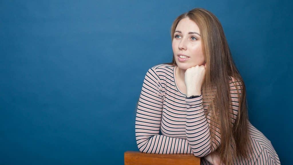 A woman wearing a striped shirt is standing while leaning on a wooden block.