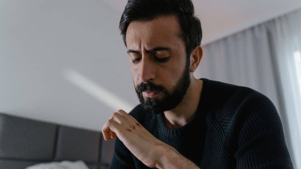 A bearded man sitting in a room looking at his hand.
