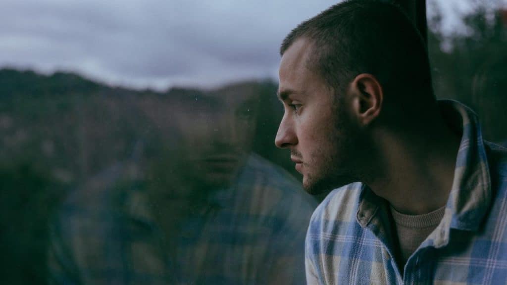 A man gazing out a window with a pensive expression.