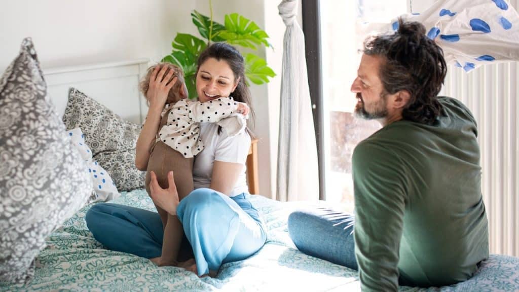 A woman holding her baby while her husband is sitting next to her on the bed.