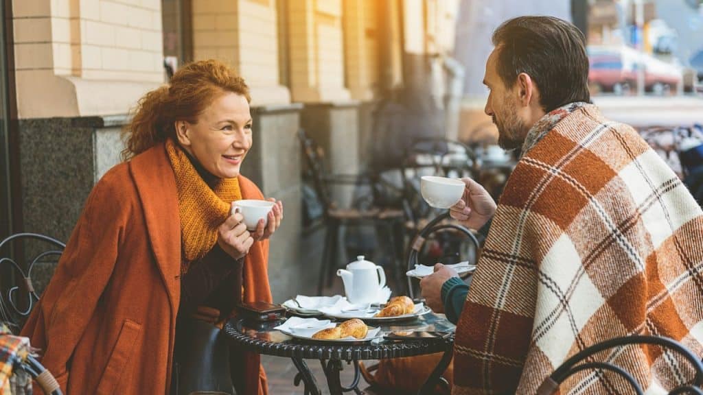 Couple is drinking tea and talking in cafe outdoors they are looking at each other with love and smiling.