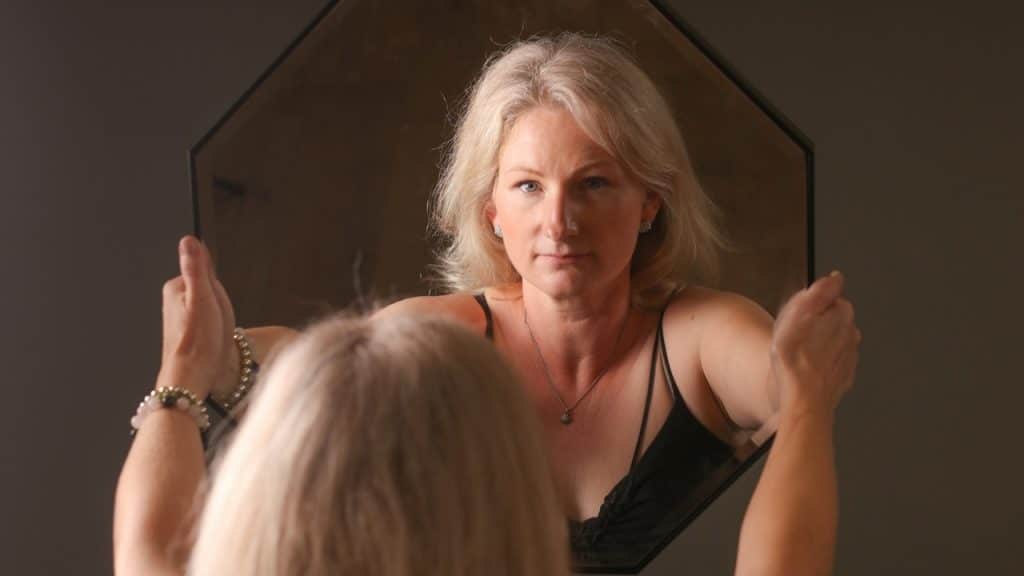 An older woman holding up a mirror and looking at her reflection.