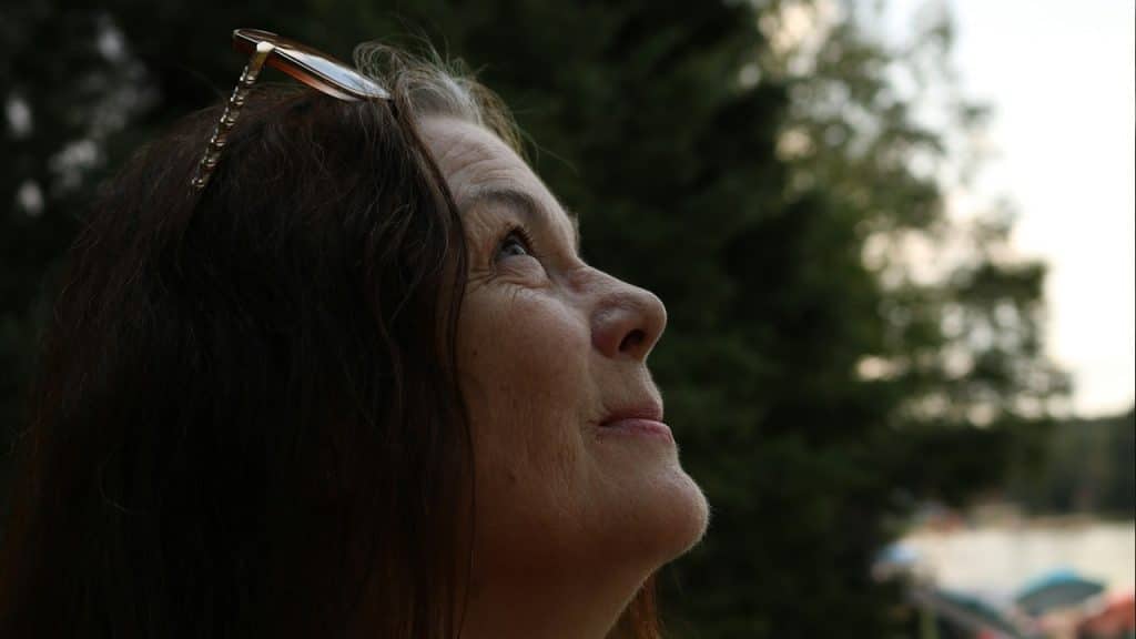 An older woman with glasses on her forehead looking up.