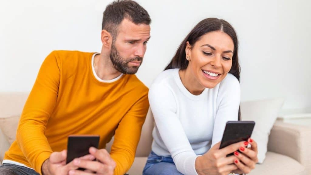 A smiling woman looks at her phone while a man beside her looks at her screen.