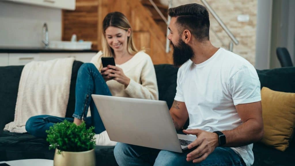 A woman smiles at her phone while a man with a laptop looks toward her.