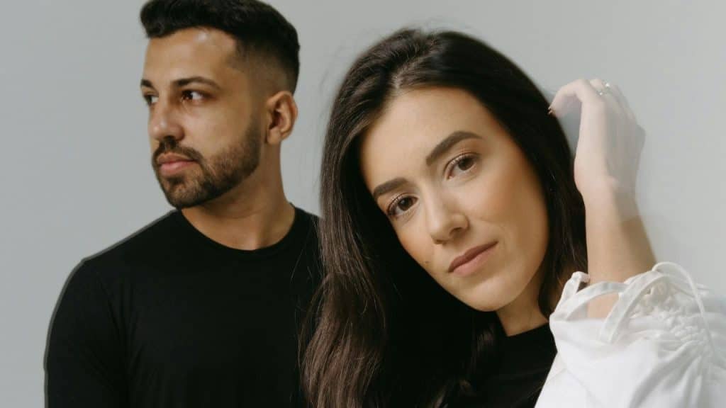 A woman looks directly at the camera while a man in a black shirt looks away.