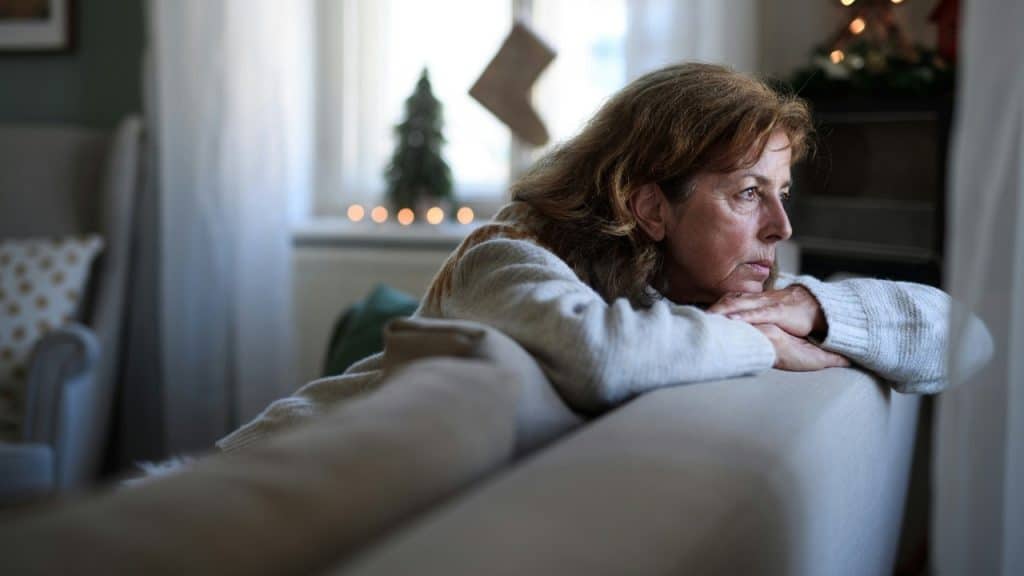 A middle-aged woman rests her chin on her hands while gazing out a window.