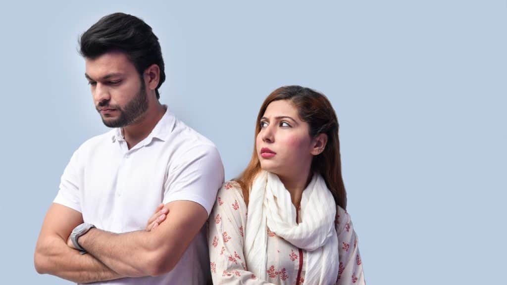 A man and woman stand back-to-back while the woman looks over her shoulder.