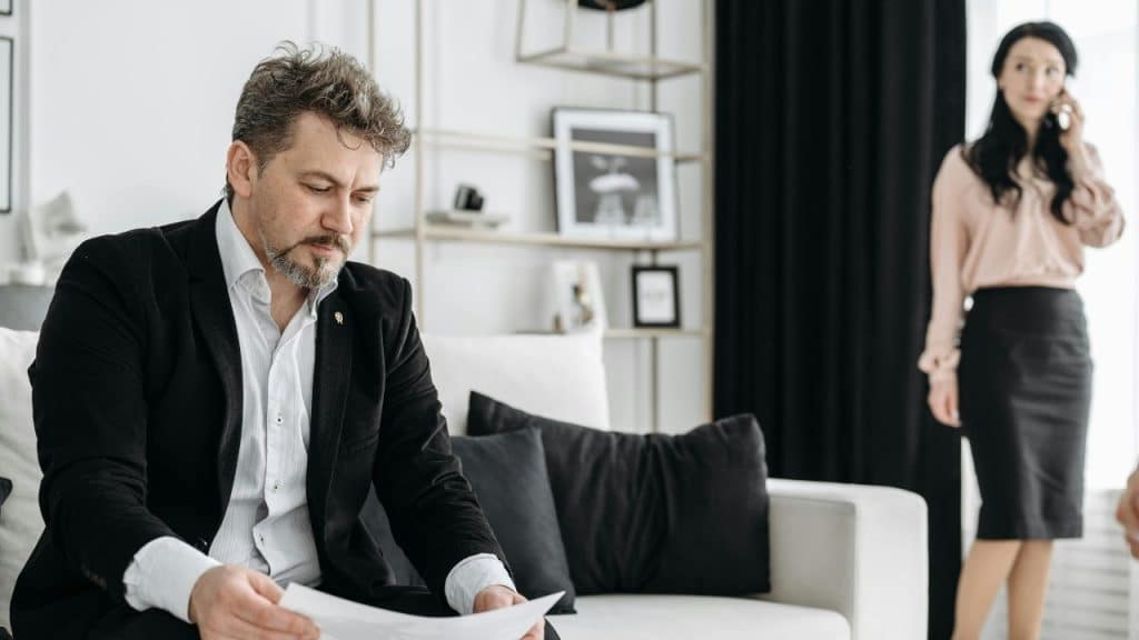 A man in a suit looks at papers while a woman talks on a phone.