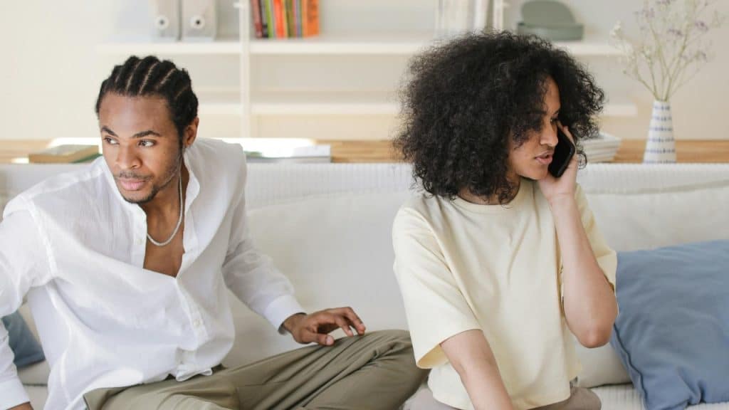 A woman talks on a smartphone while a man sits beside her looking away.