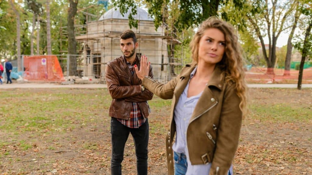 A woman raises her hand in a stopping gesture while a man watches her.