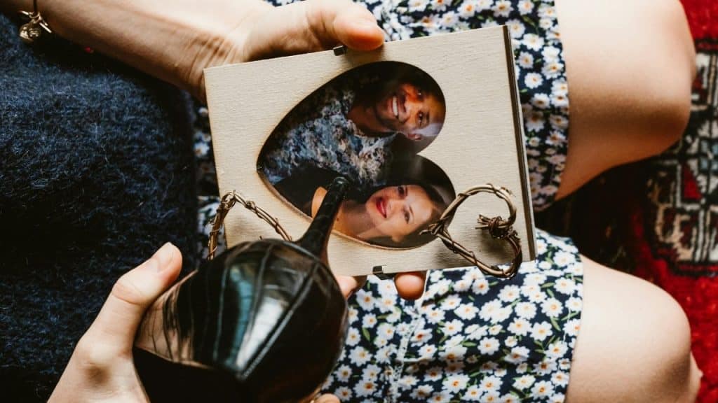 A person holding a heart-shaped wooden frame containing a photo of a smiling couple.
