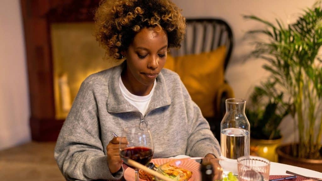 A woman with curly hair sits at a table eating a meal with wine.