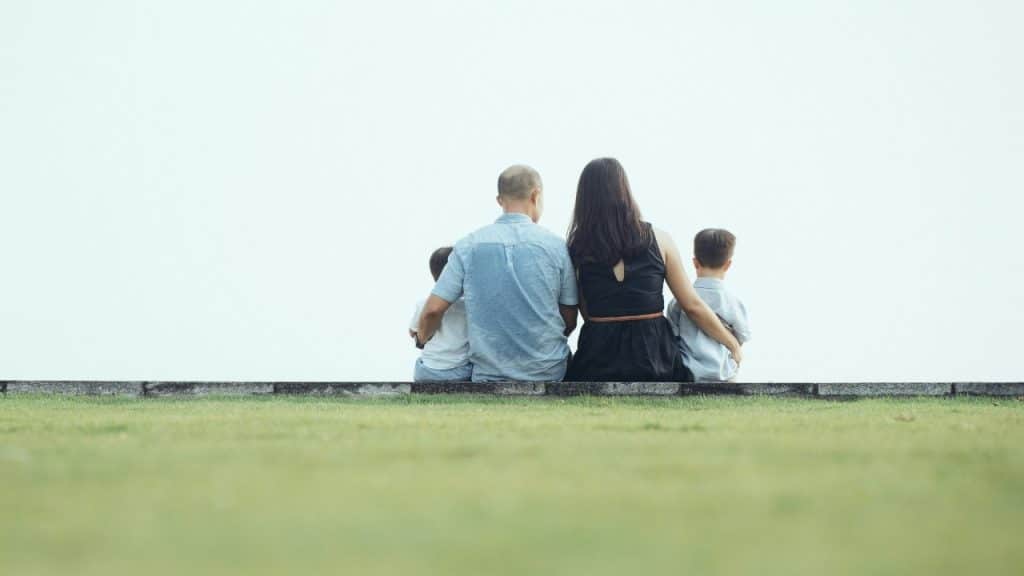 A man, a woman, and two children sitting on a ledge with their backs to the camera.