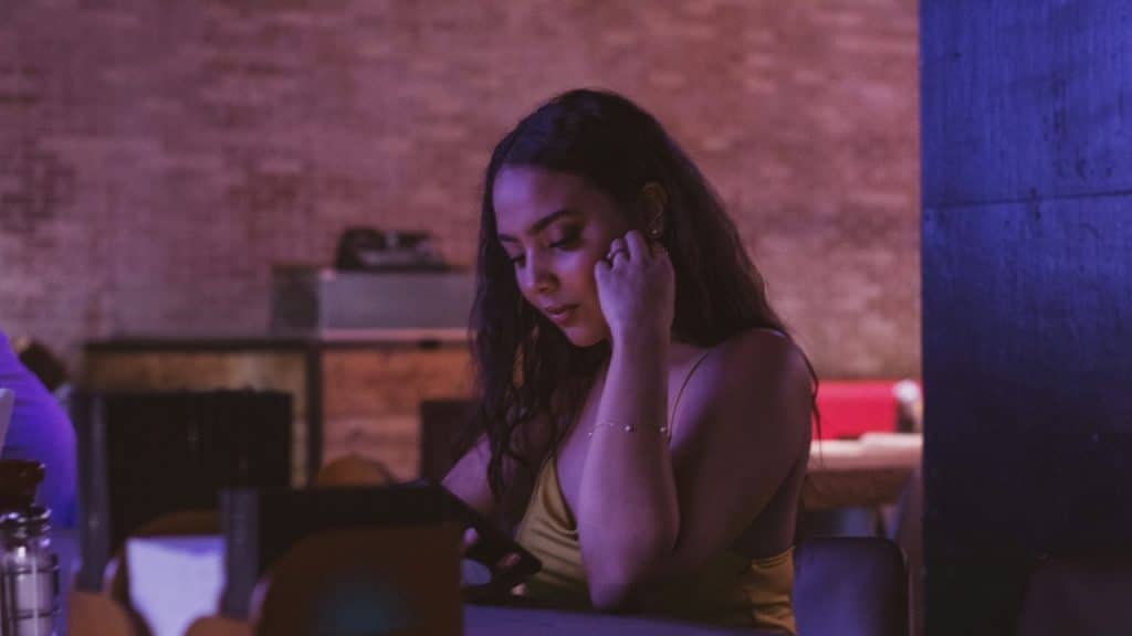 A woman with long dark hair looking down at a phone in a dimly lit, purple-toned room.