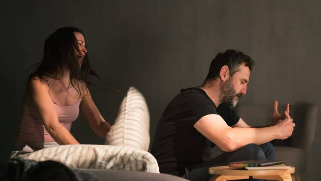 A woman shouts and gestures while a man sits looking down with his head bowed.