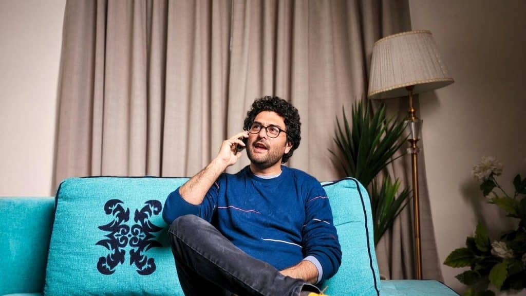 A man sitting on a couch talking on his phone in a living room.