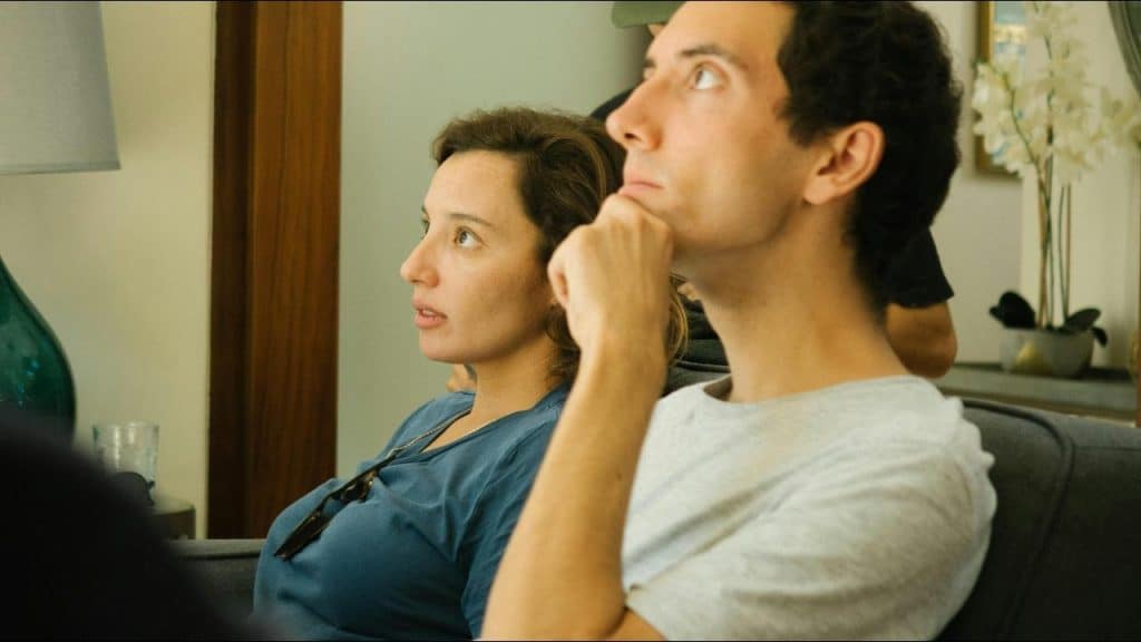 A man and woman sitting on a couch, looking focused at something off-camera.