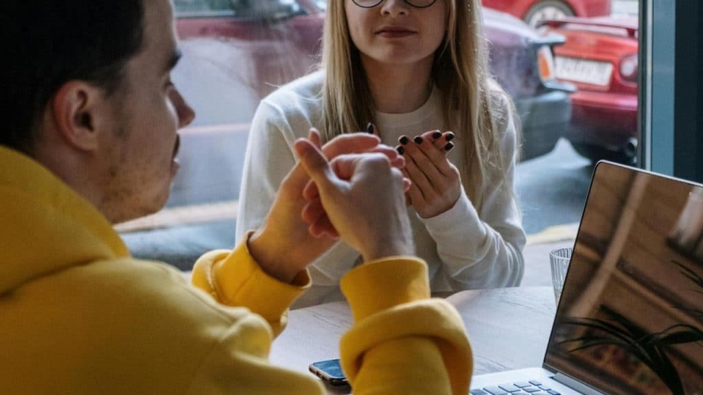 A man and woman having a discussion at a table with a laptop in a café.