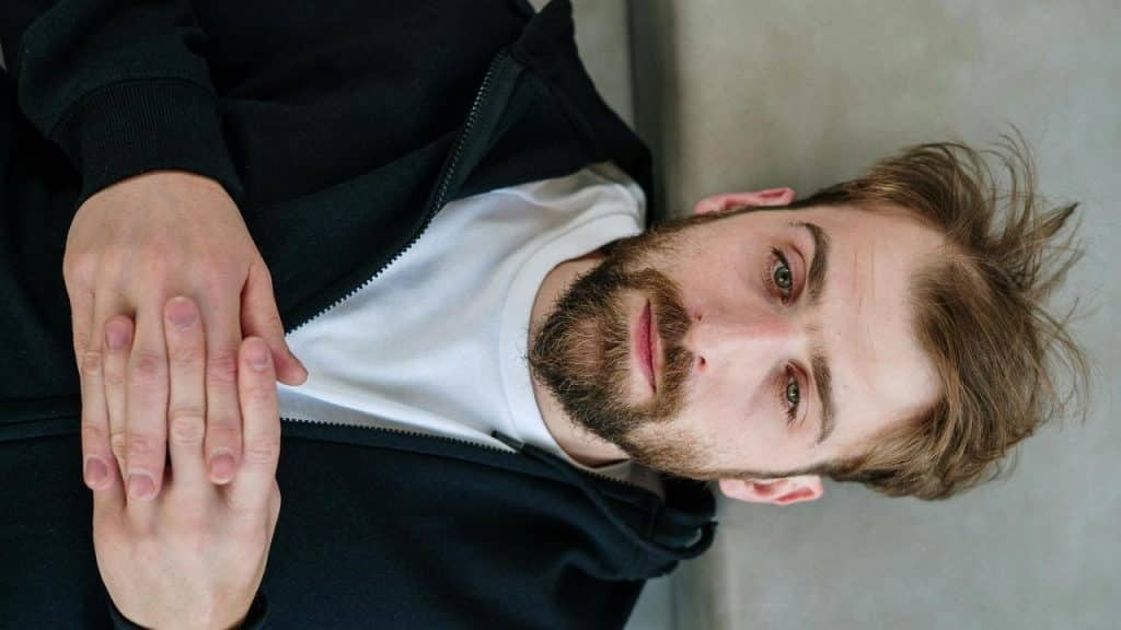 A man lying down with his hands clasped, looking thoughtful.
