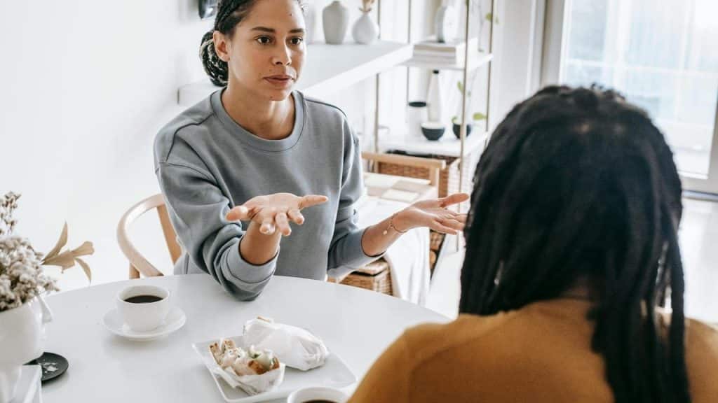 A person gesturing while talking to another person at a table with coffee.