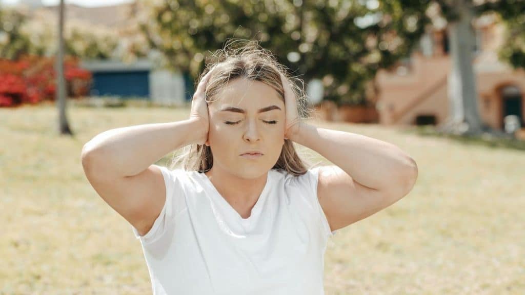 A woman outdoors covering her ears with her eyes closed.