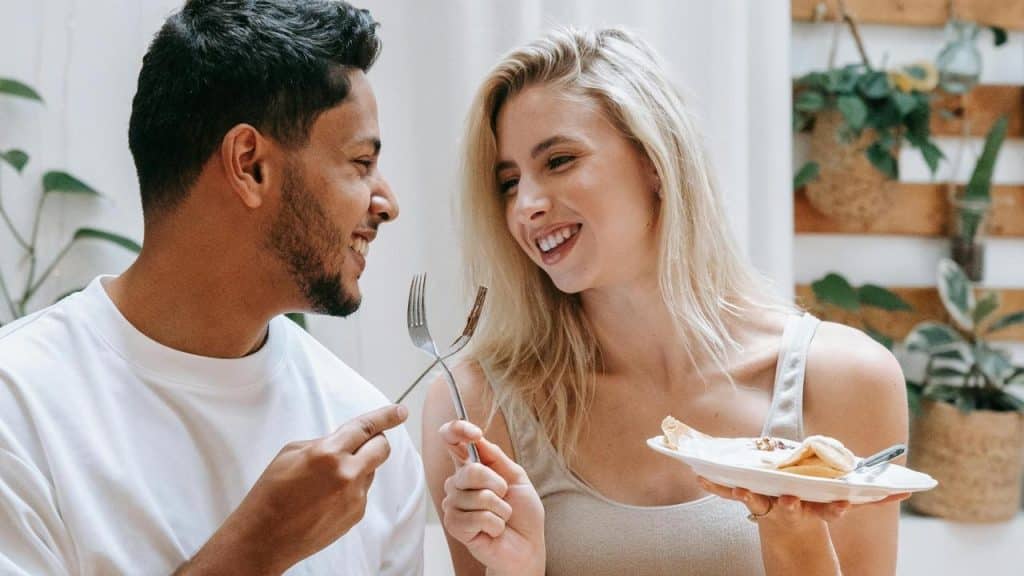 A couple smiling at each other while sharing dessert and holding forks.