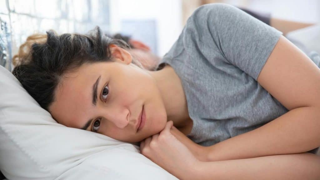 A woman lying on a pillow, looking ahead with a tired or pensive expression.