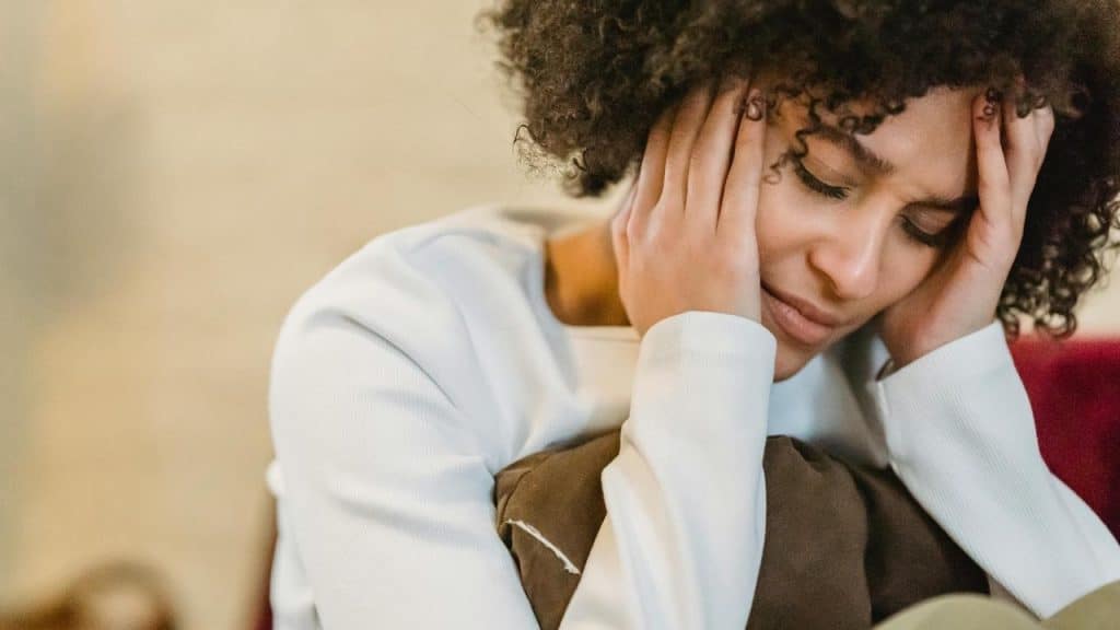 A person holding their head with both hands, eyes closed in distress.